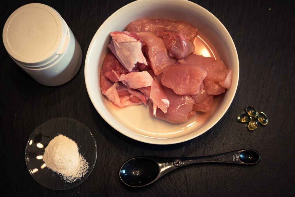 A white bowl with raw meat on a dark wooden table with a black spoon, to prepare a raw cat food diet.