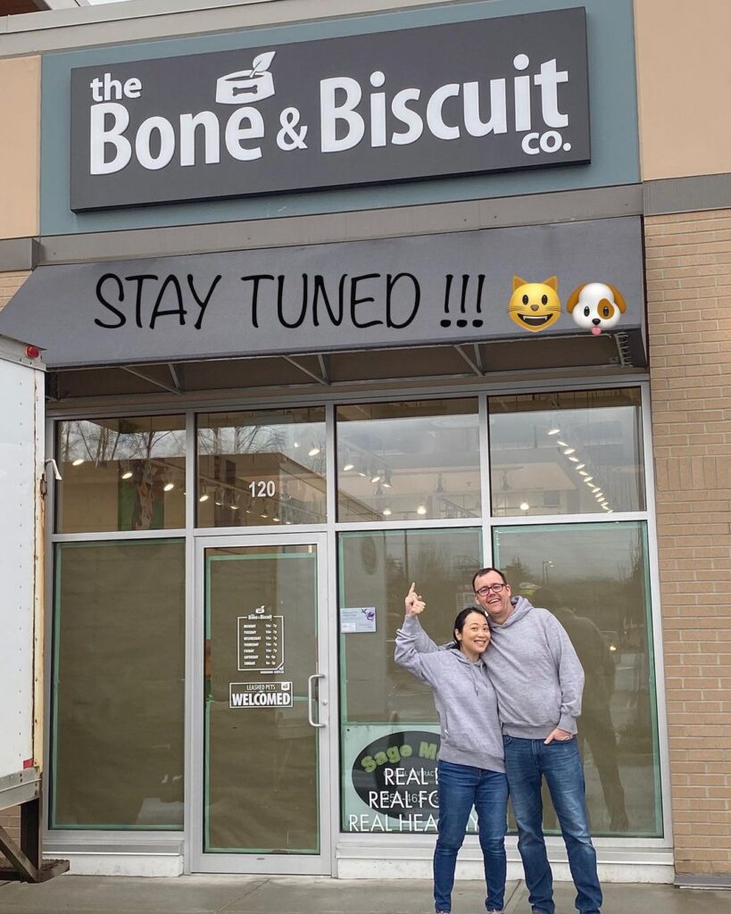 Man and woman in jeans and grey sweatshirts stand outside of The Bone & Biscuit in Maple Ridge