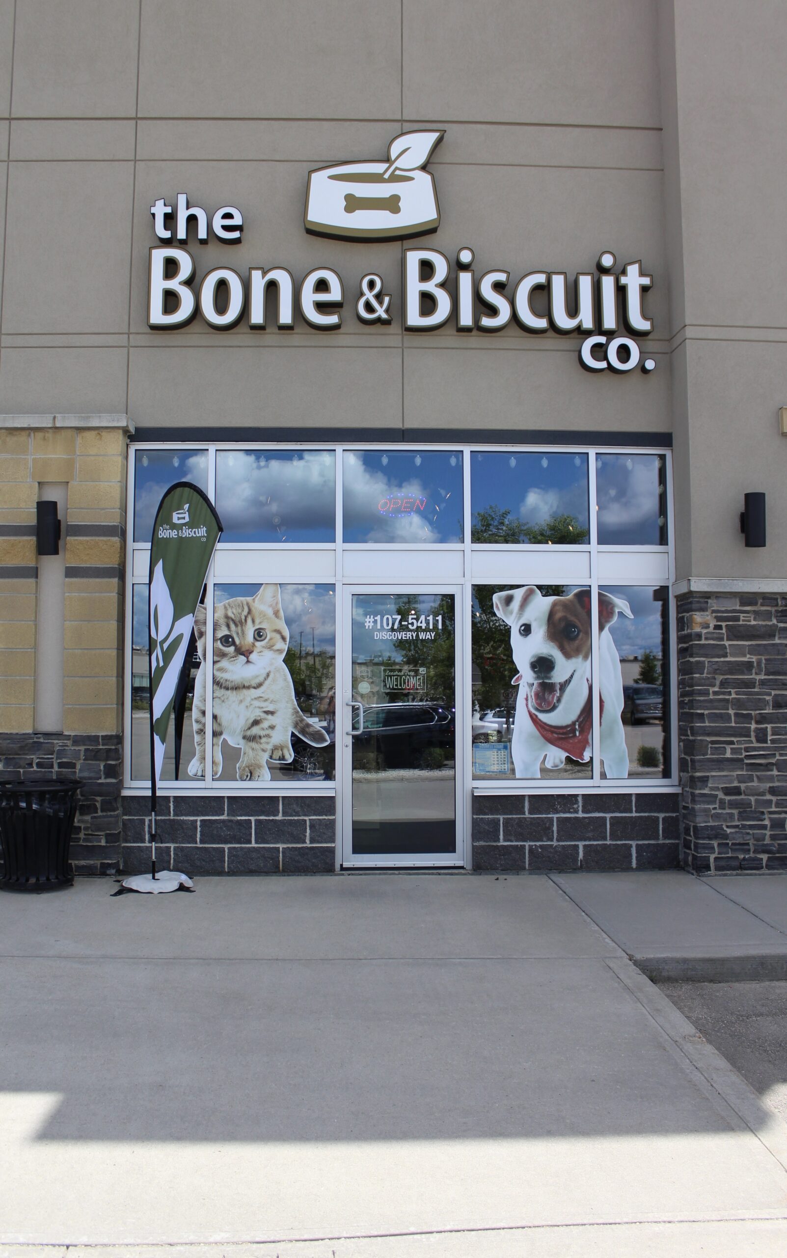 The storefront of the Bone & Biscuit Leduc location with large glass windows and a photo of a cat and a dog on the front of the store.