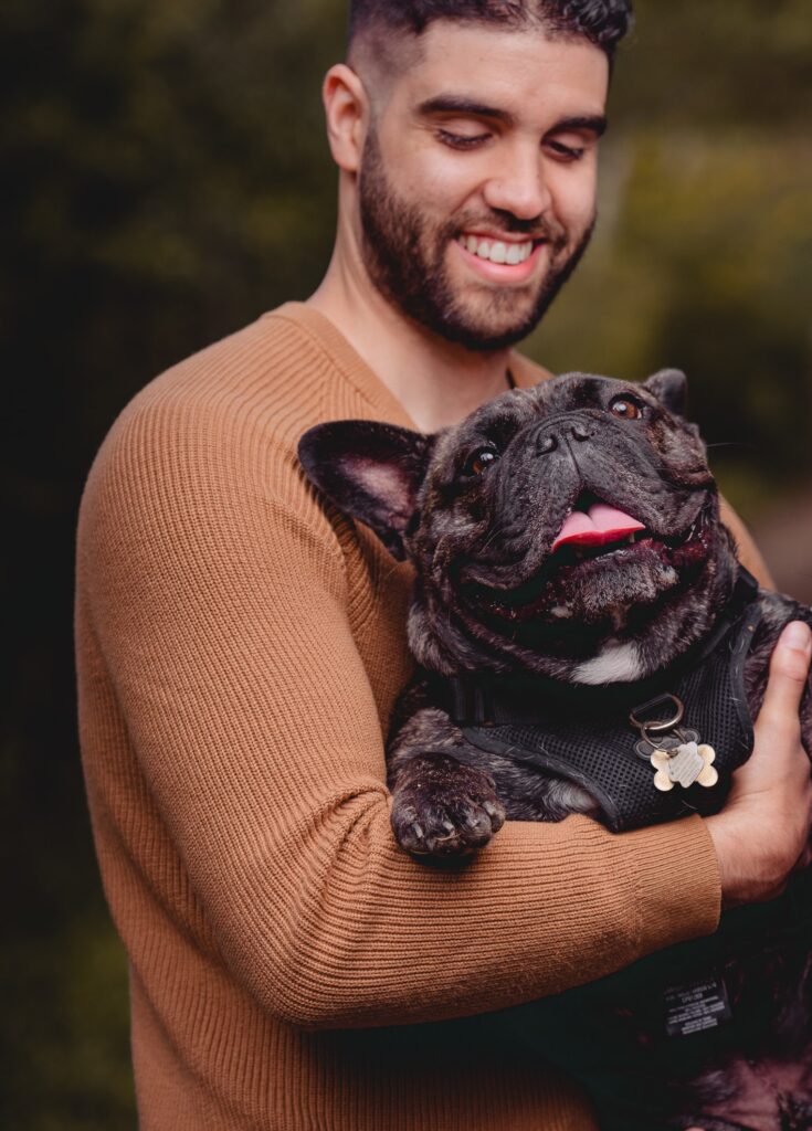 Christopher, one of the store owners of the Bone & Biscuit Yonge Sheppard Location, smiles and holds his french bulldog mix, Gordy, while outside in a park in North York, Ontario.