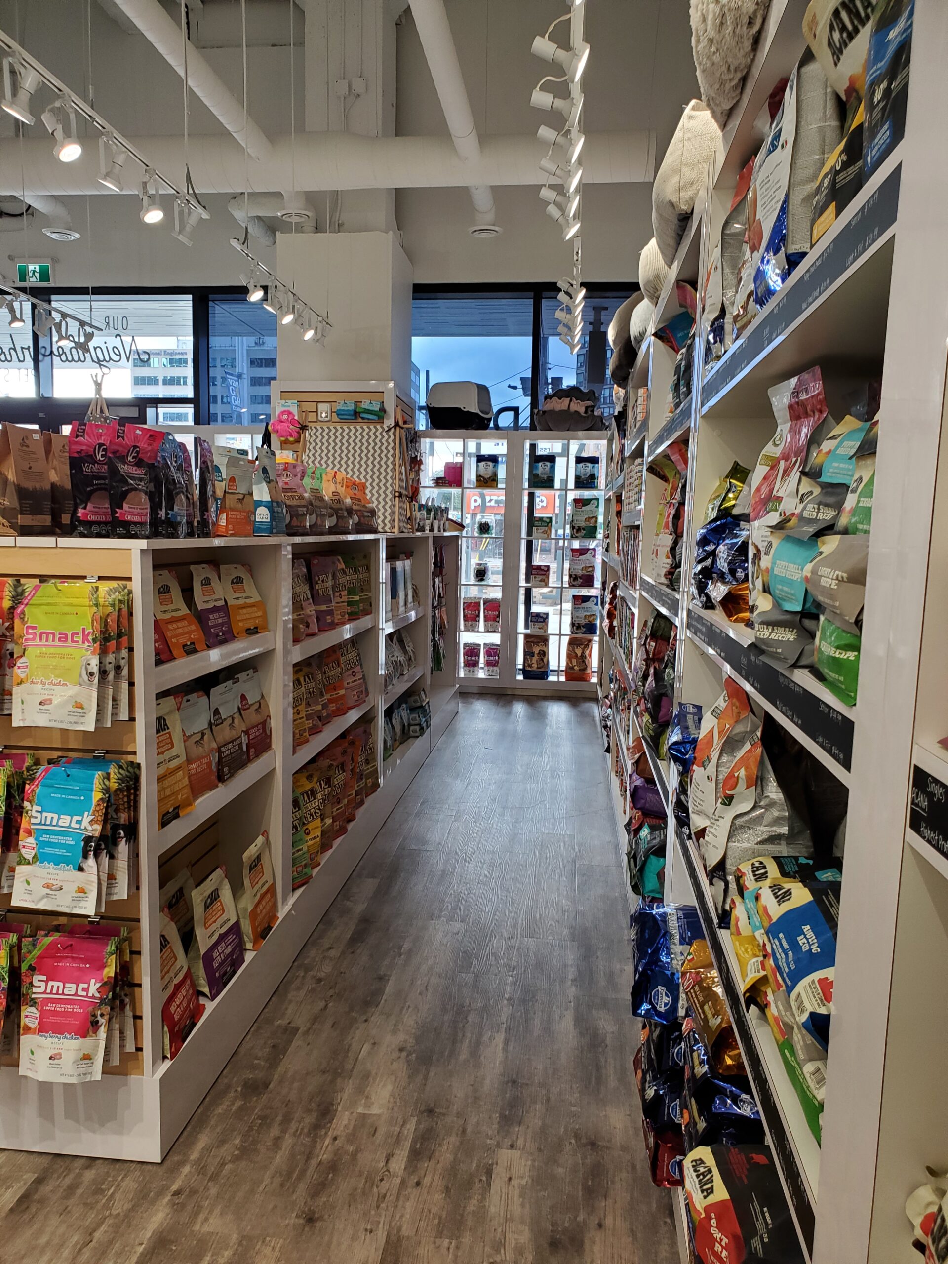 Inside the Bone & Biscuit Yonge Sheppard store, displaying it's wood-style floors and shelves of dog food, cat food and pet treats in a brightly lit store.