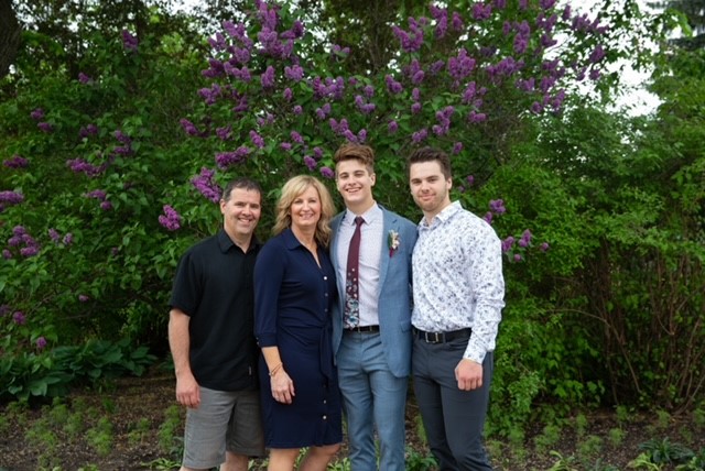 Bone & Biscuit Riverside owner, Tara, and her family, including her husband and two sons, standing in front of a lilac bush for a family photo in St. Albert.