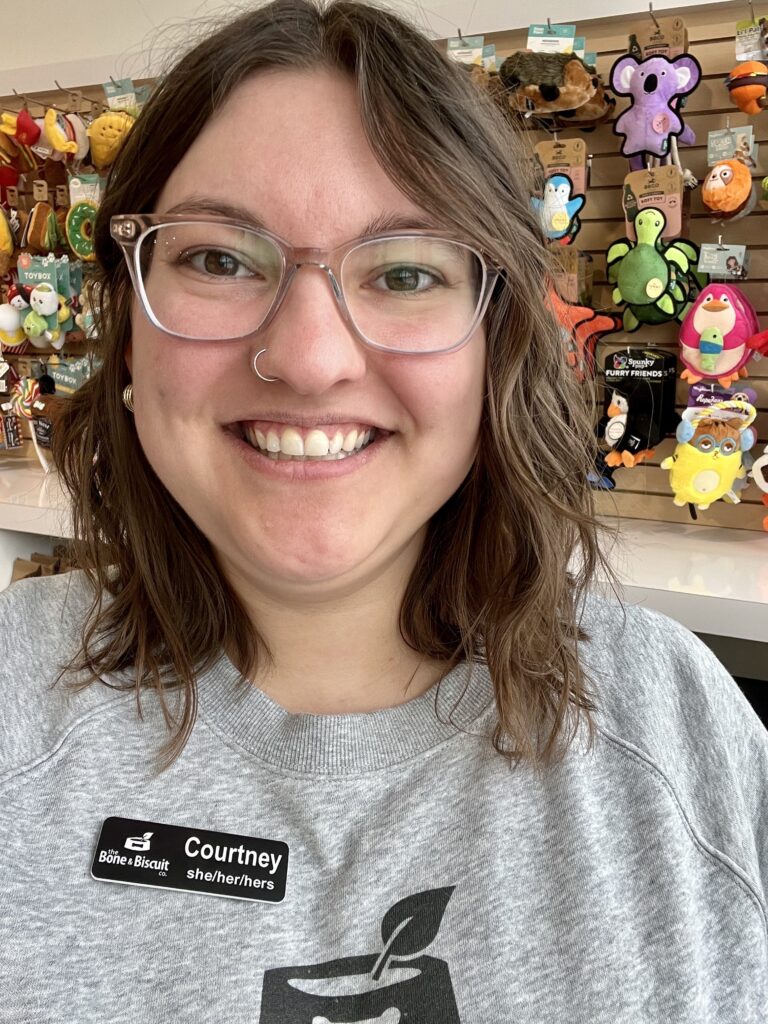 Bone & Biscuit Garneau's owner, Courtney, smiles with glasses and a name tag on while inside her pet supply store in Edmonton, Alberta.