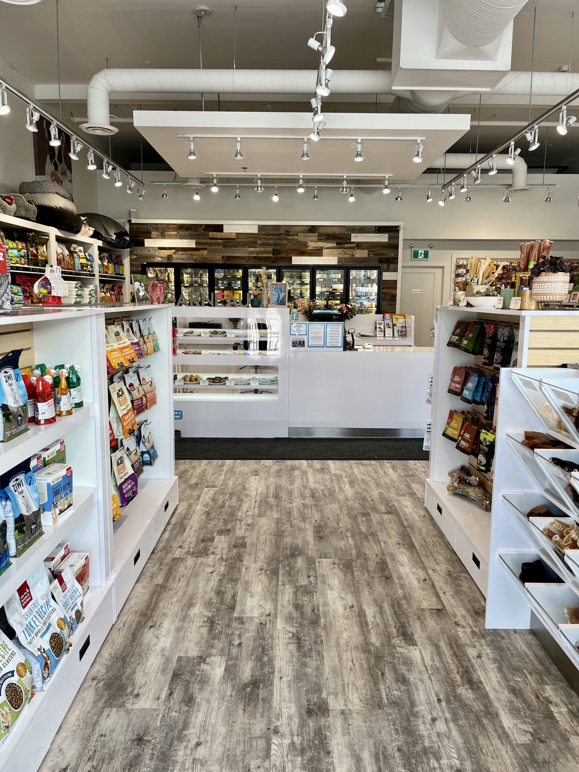 Shelves with dog treats and cat treats, as well as the front counter in the background, inside the brightly lit, nicely decorated Bone & Biscuit Garneau location, a pet supply store in Edmonton, Alberta.