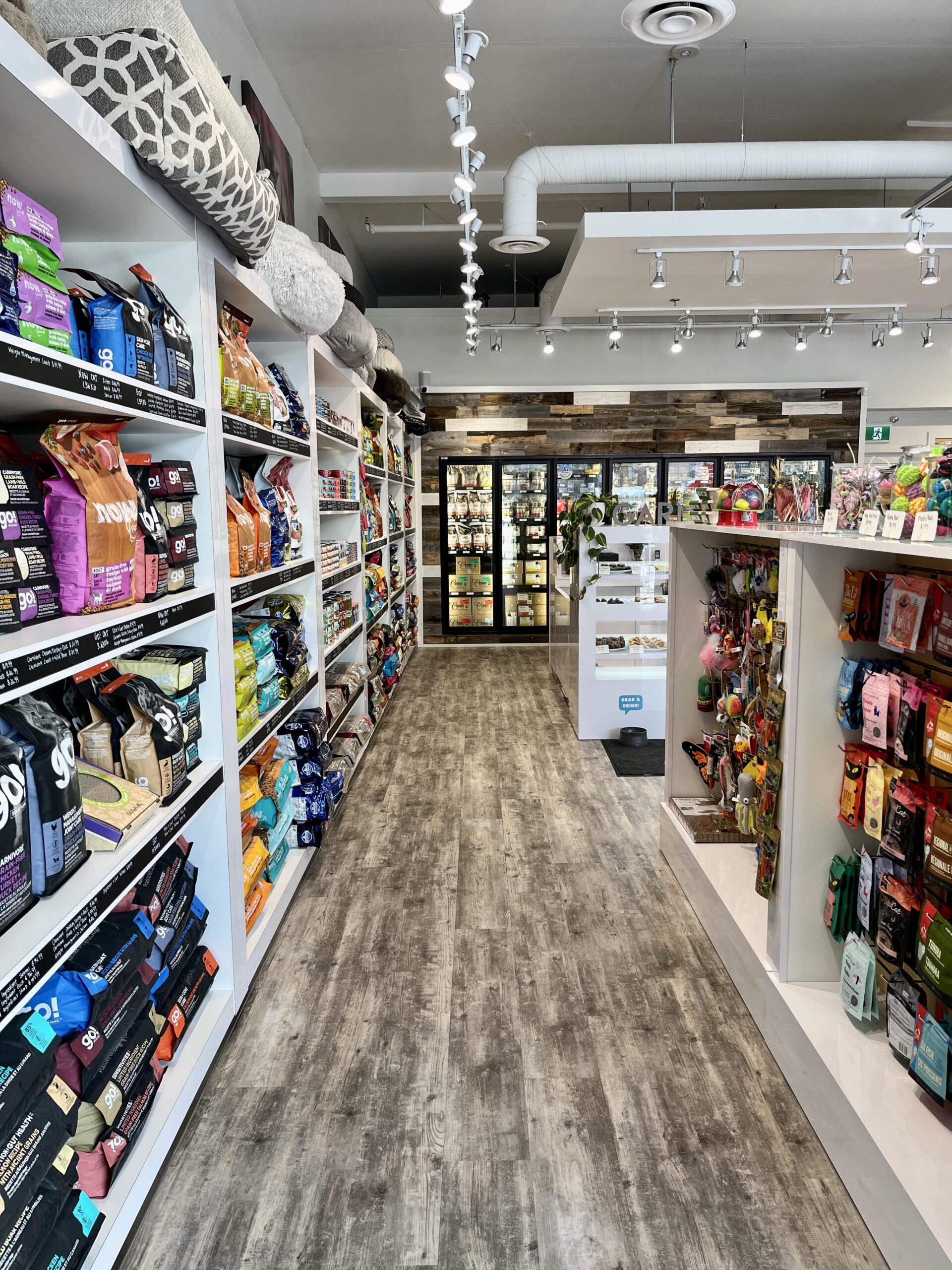 Shelves with dog treats and dog food inside the brightly lit, nicely decorated Bone & Biscuit Garneau location, a pet supply store in Edmonton, Alberta.