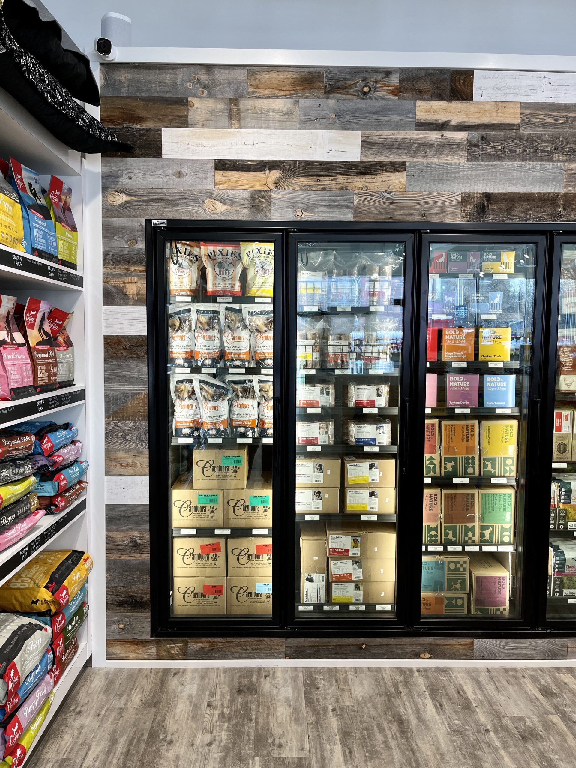 The freezer and fridge shelves with dog and cat treats and food inside the brightly lit, nicely decorated Bone & Biscuit Garneau location, a pet supply store in Edmonton, Alberta.