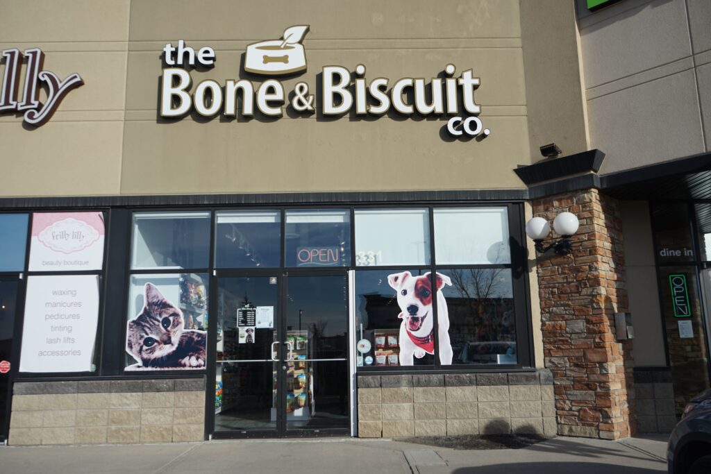 The outside of Bone & Biscuit Okotoks' store front on a sunny day, a pet supply store near Calgary in Alberta.
