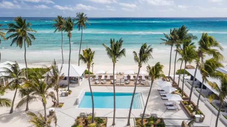 Rectangular pool at Caerula Mar Club, South Andros, Bahamas, with palm trees, cabanas, and ocean views under a partly cloudy sky.