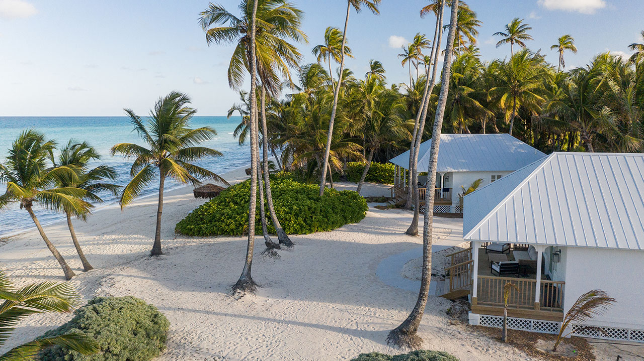 White sand beach, palm trees, turquoise sea, and elegant cottage at Caerula Mar Club, luxury resort on South Andros Island, Bahamas.