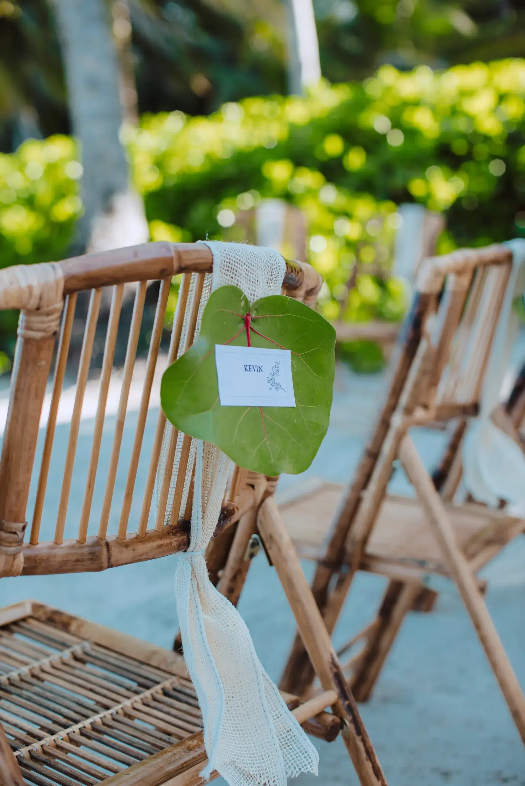 Elegant bamboo chair with white fabric and leaf decor, card labeled "KEVIN," outdoors at Caerula Mar Club, South Andros, Bahamas.
