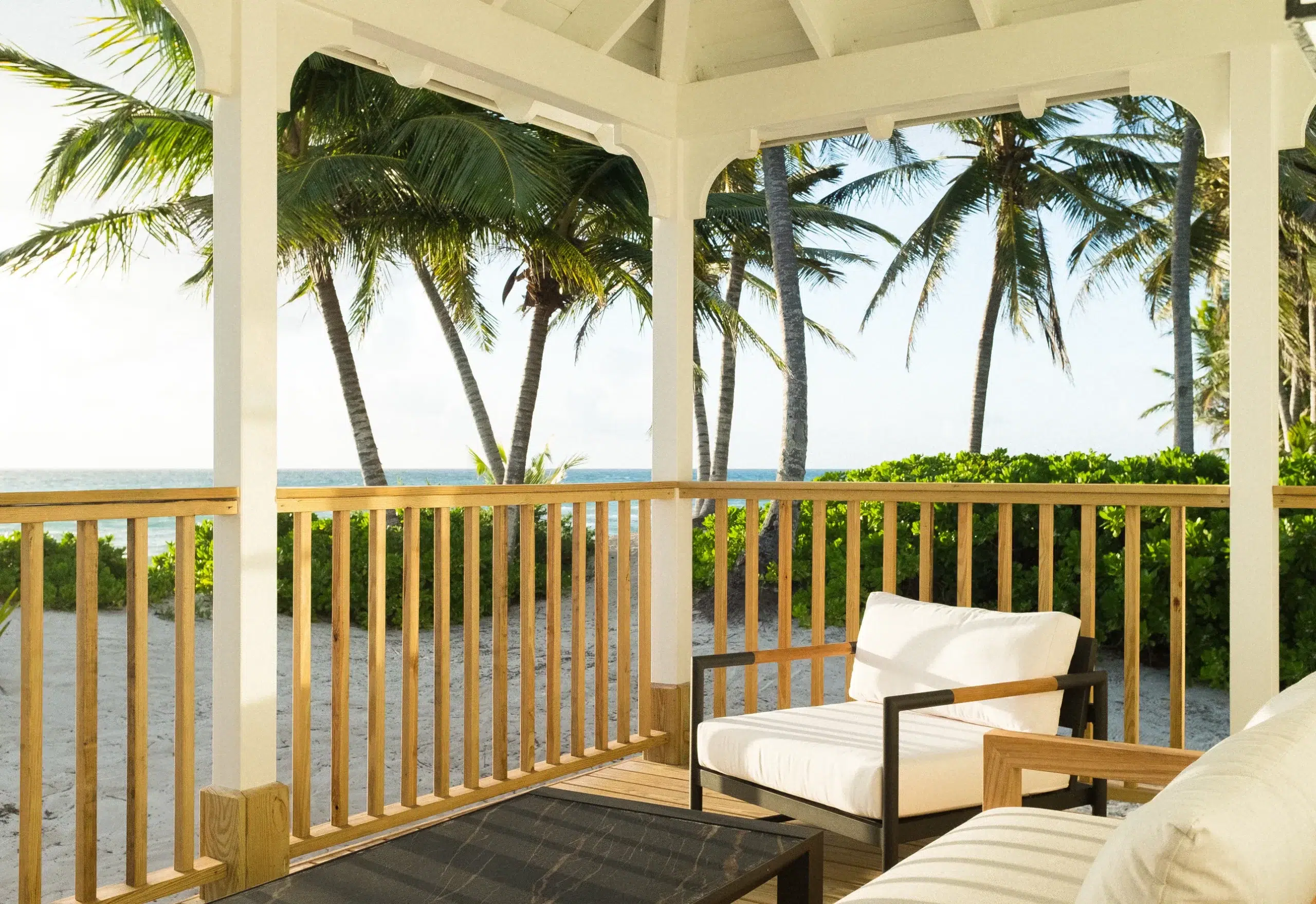 Beachfront porch at Caerula Mar Club with white cushioned chairs, ocean views, palm trees, and sand on South Andros Island, Bahamas.