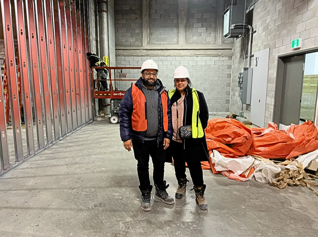 Jas and Sunil, the owners of the new Bone & Biscuit the Well pet store in downtown Toronto, stand in safety vests and helmets in the under-construction pet store.