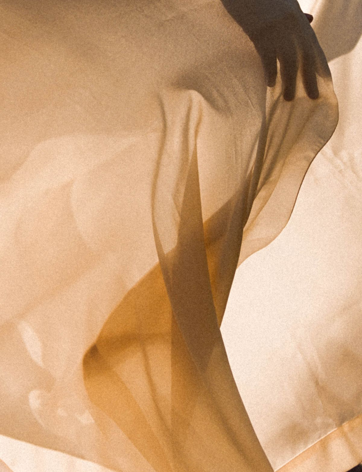 Hand holding flowing beige fabric with soft light and shadows at Caerula Mar Club, luxury resort on South Andros Island, Bahamas.